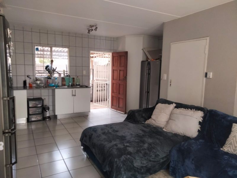 Open plan living area featuring tiled flooring and a functional kitchen space with cabinetry and sink, leading to an exterior access point.
