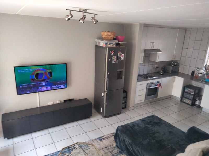 Open-plan living area featuring a compact kitchen with built-in appliances and tiled flooring, seamlessly connected to the lounge space.