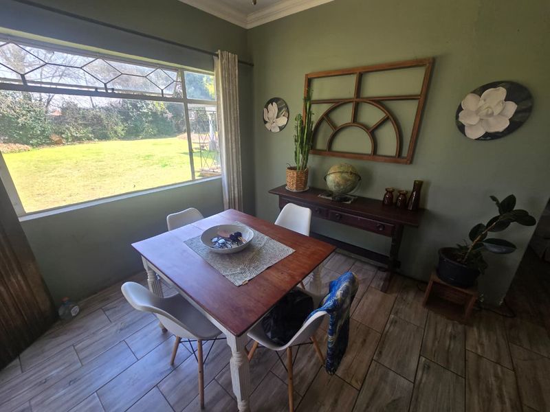 A dining room featuring wood-look tile flooring, crown molding, and a large window overlooking the garden.