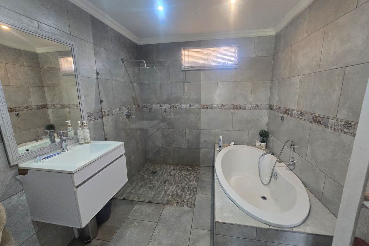 Modern bathroom featuring a walk-in shower, a sleek freestanding bathtub, and a contemporary vanity unit with grey tiled finishes throughout.
