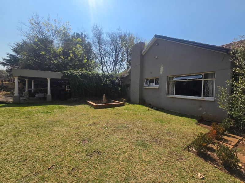 Rear view of the property featuring a lawn, a masonry fountain, and a covered patio area attached to the main building structure.