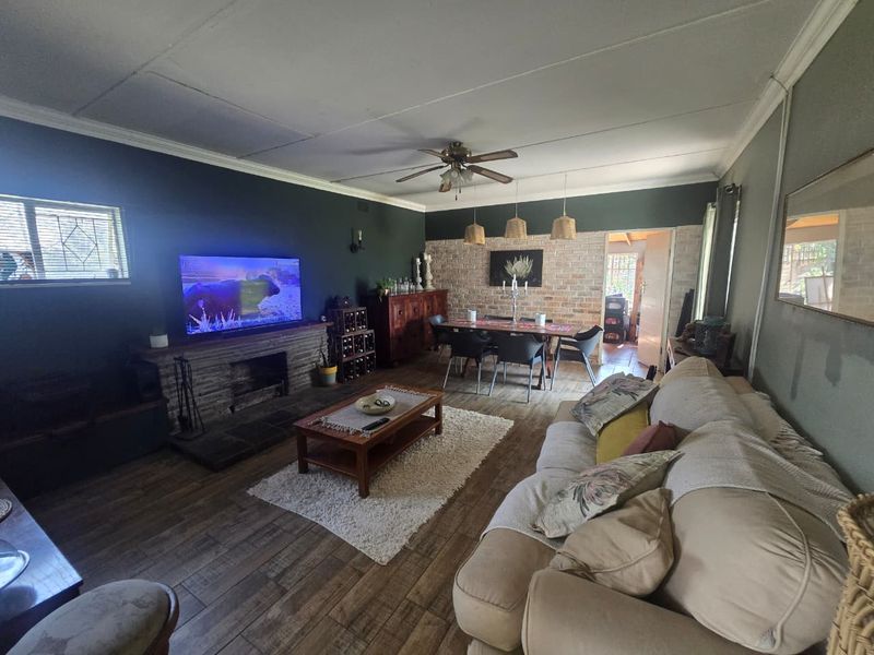 Open plan living and dining area featuring a stone fireplace, exposed brick wall, ceiling fan, and tiled flooring.