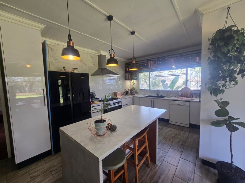 Modern kitchen featuring a central island, gas hob with extractor, double sink, and ample built-in cabinetry with contemporary finishes.