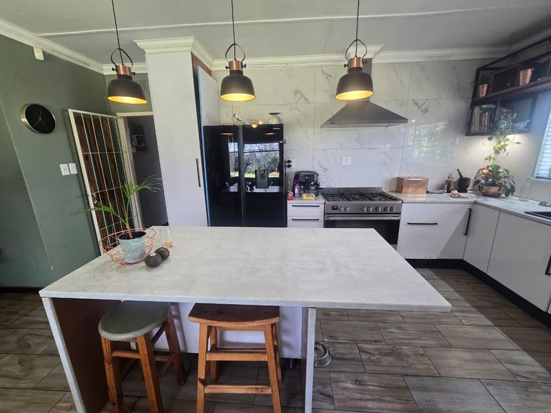 Modern kitchen featuring a central island, gas stove with extractor fan, marble-look splashback tiles, and contemporary pendant lighting.