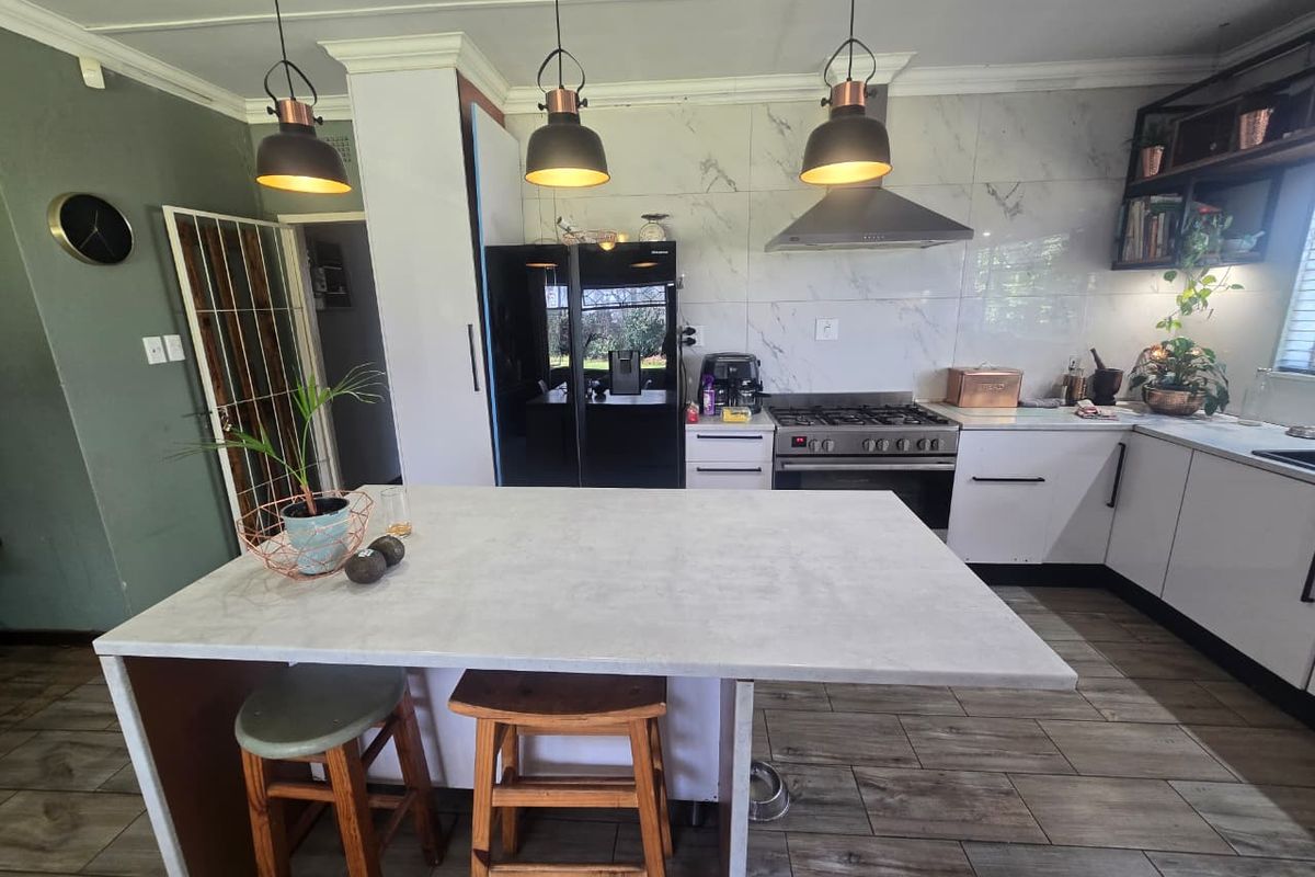 Modern kitchen featuring a central island, gas stove with extractor fan, marble-look splashback tiles, and contemporary pendant lighting.