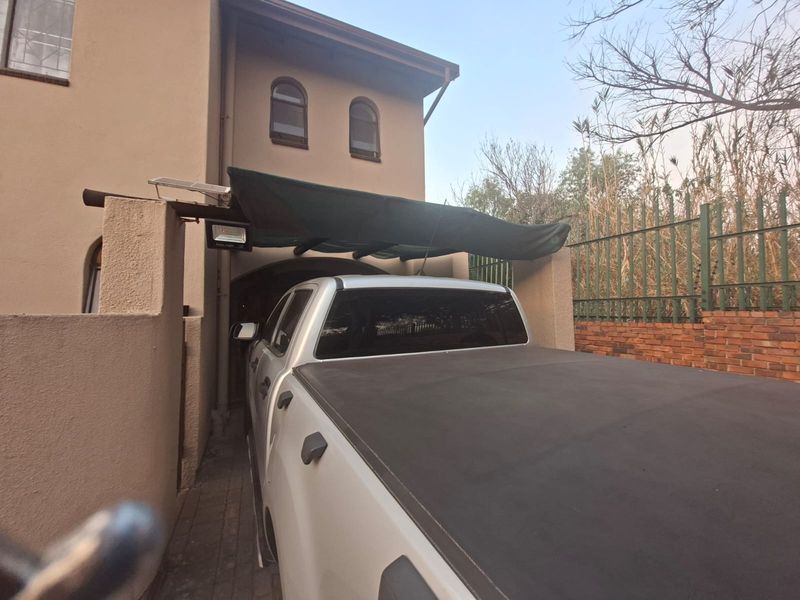 Front exterior view of the townhouse featuring a paved driveway, a shade cloth carport, and perimeter security fencing.