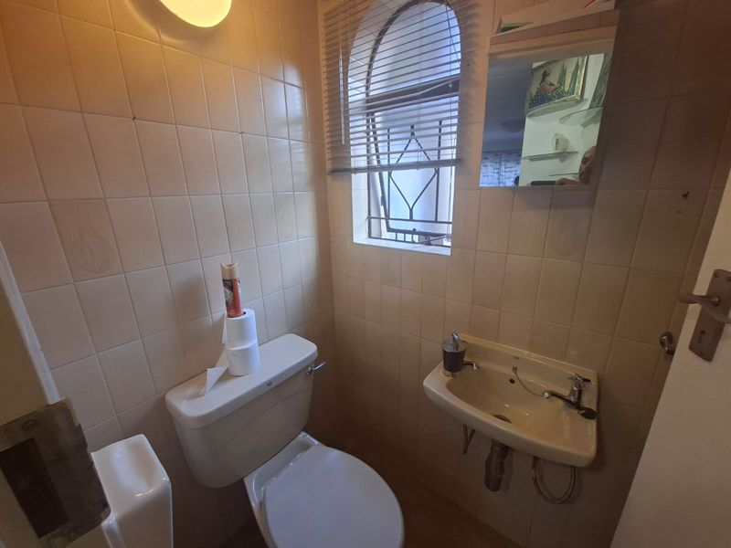 A compact guest bathroom featuring dated wall tiles, a wall-mounted basin, and a toilet, with an arched window providing natural light.