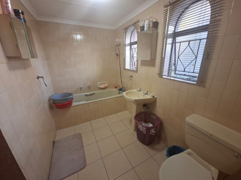 A functional bathroom featuring a bathtub, pedestal basin, and toilet with neutral tiled finishes and security bars on the windows.