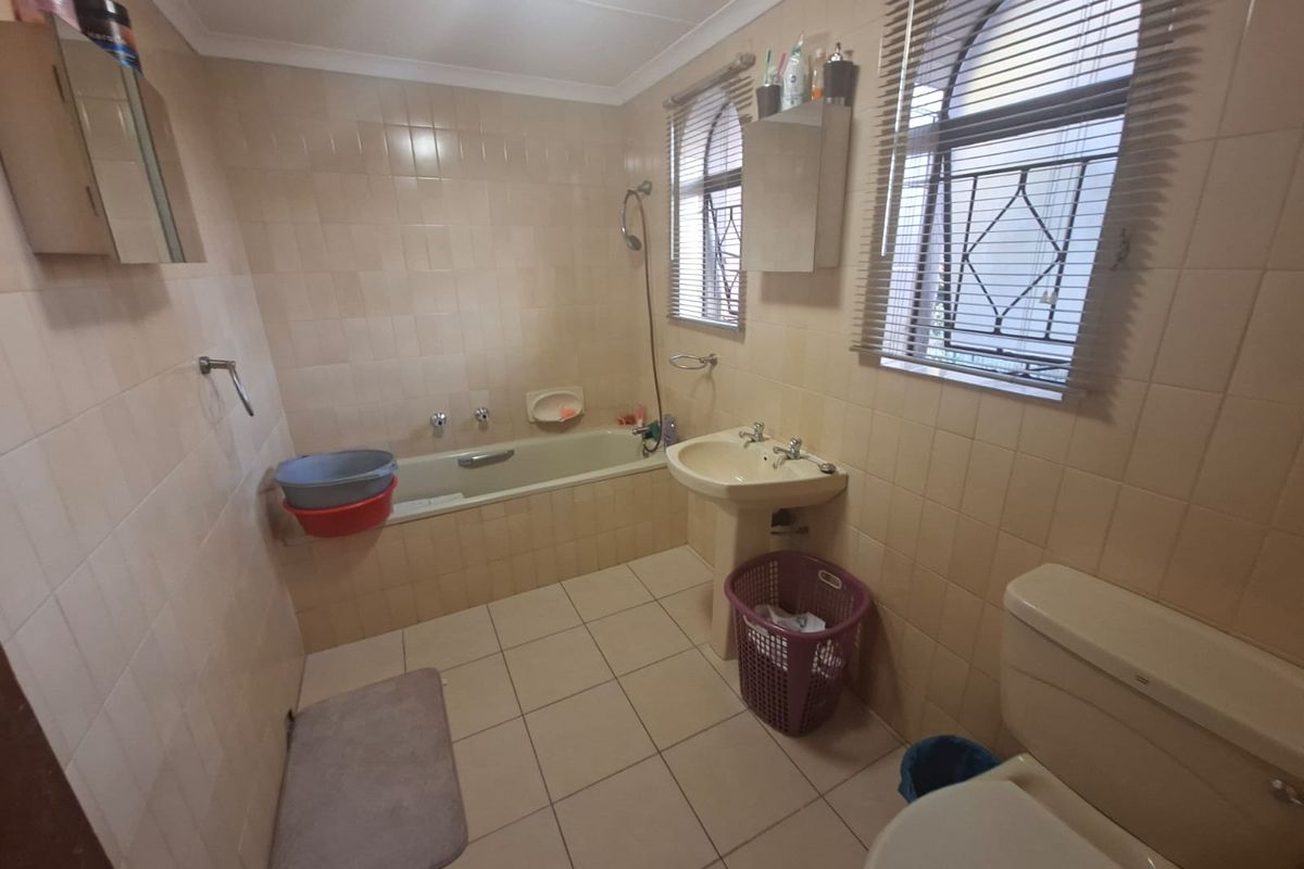 A functional bathroom featuring a bathtub, pedestal basin, and toilet with neutral tiled finishes and security bars on the windows.