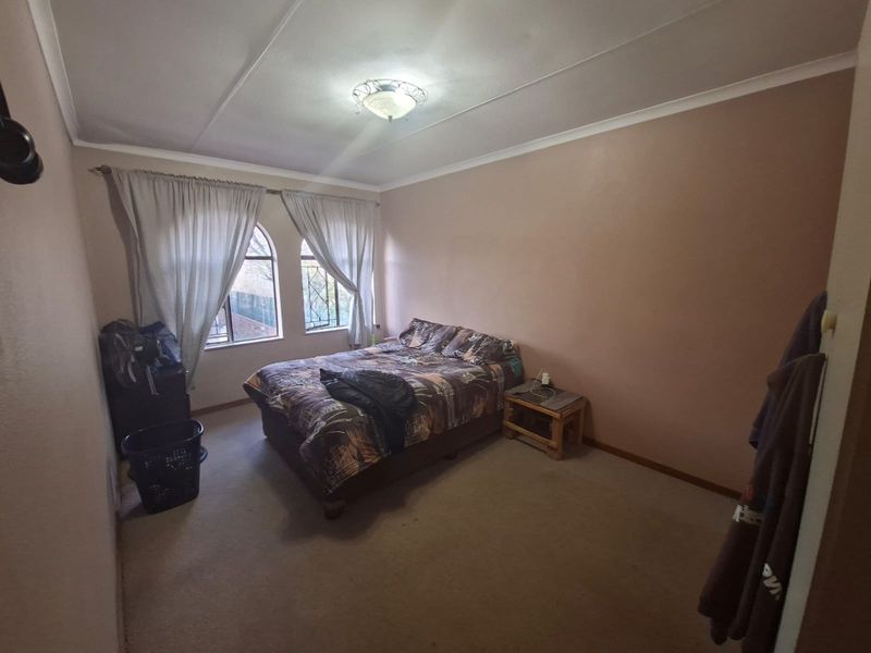 A bedroom featuring arched windows with security bars, carpeted flooring, and a central ceiling light fixture.