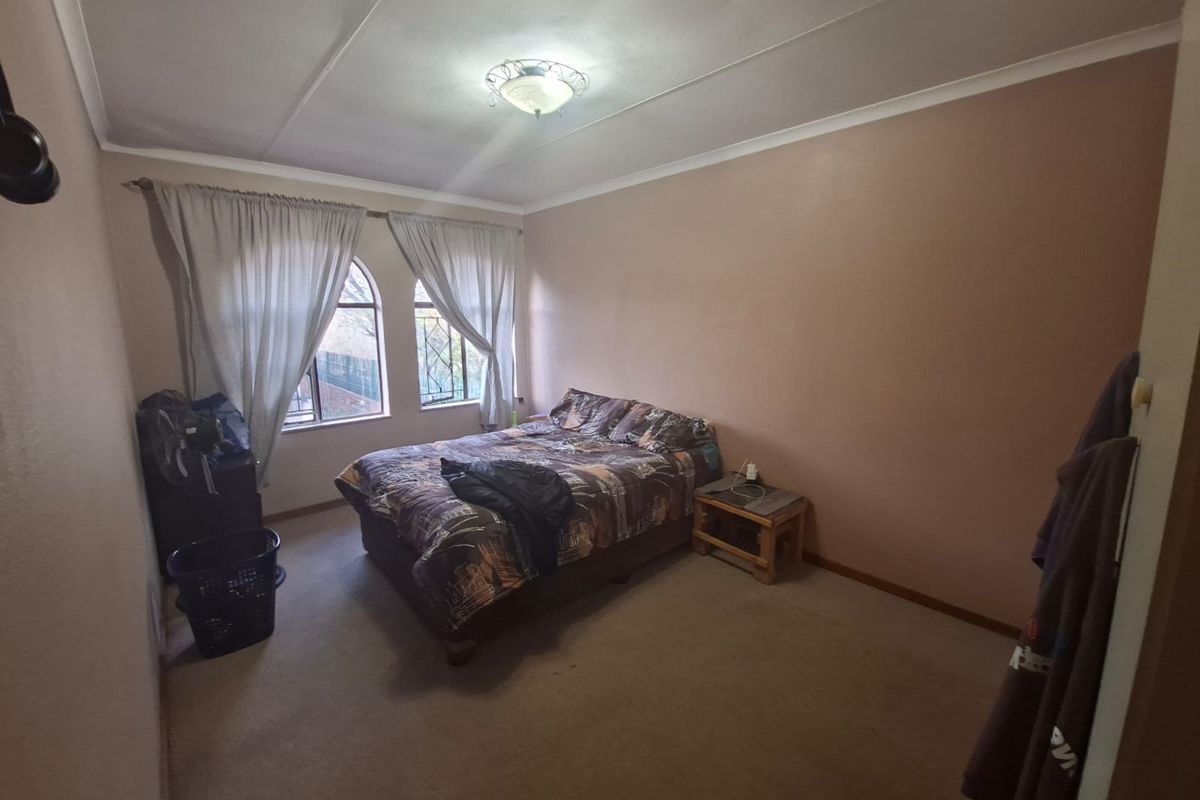 A bedroom featuring arched windows with security bars, carpeted flooring, and a central ceiling light fixture.