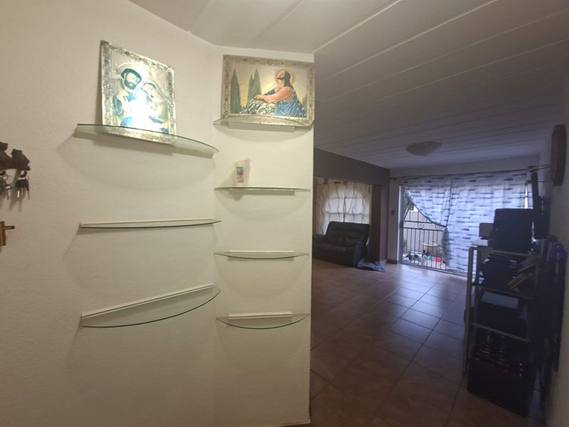 A living area featuring tiled flooring, wall-mounted glass shelving, and a sliding door providing access to an outdoor space.