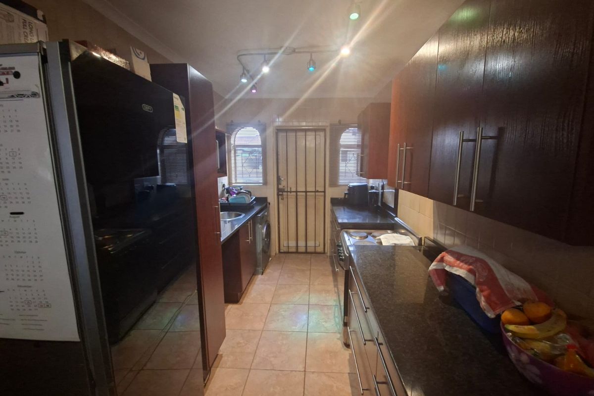 A functional galley-style kitchen featuring dark wood cabinetry, granite countertops, tiled flooring, and direct access to the exterior via a security gate.