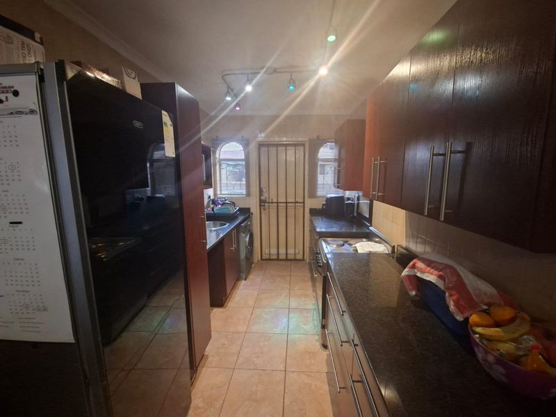 A functional galley-style kitchen featuring dark wood cabinetry, granite countertops, tiled flooring, and direct access to the exterior via a security gate.
