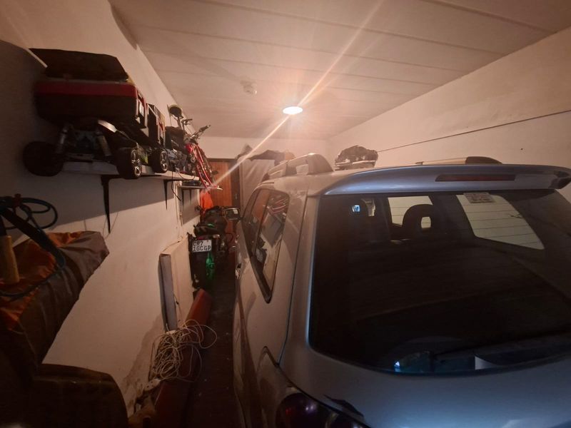 A functional garage space featuring wall-mounted shelving and overhead lighting, currently utilized for vehicle and equipment storage.