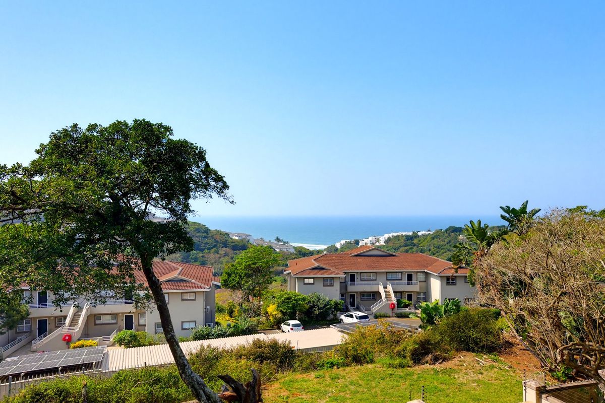 A scenic elevated view overlooking the apartment complex grounds, surrounding coastal vegetation, and the distant ocean horizon.