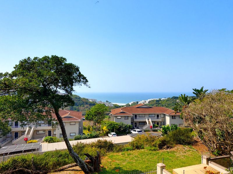 A scenic elevated view overlooking the apartment complex grounds, surrounding coastal vegetation, and the distant ocean horizon.