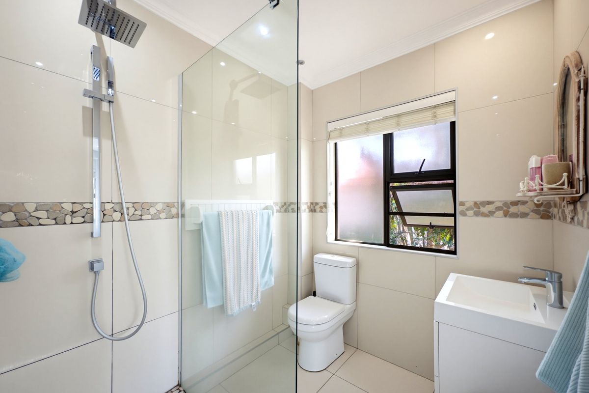 Modern bathroom featuring a glass-enclosed walk-in shower with rain shower head, contemporary vanity, and neutral tiled finishes with decorative pebble accents.
