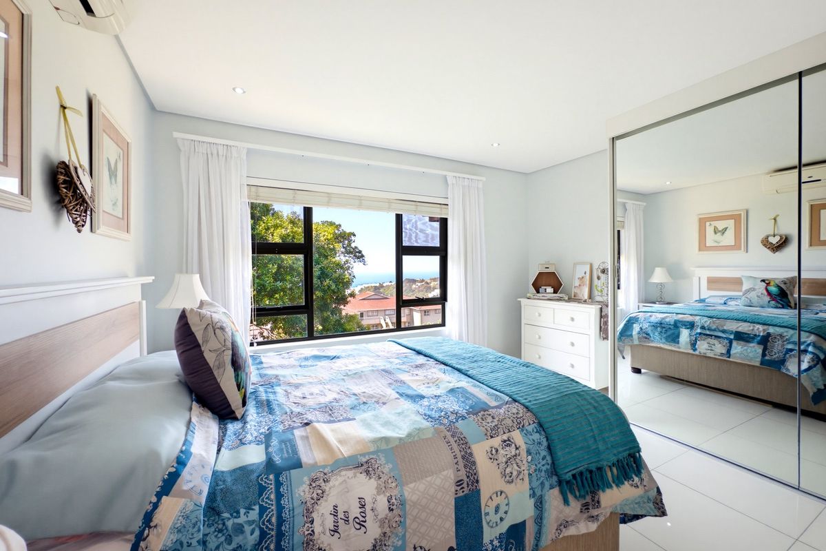 A bright bedroom featuring tiled flooring, recessed lighting, a split-system air conditioner, and a large built-in wardrobe with mirrored sliding doors.
