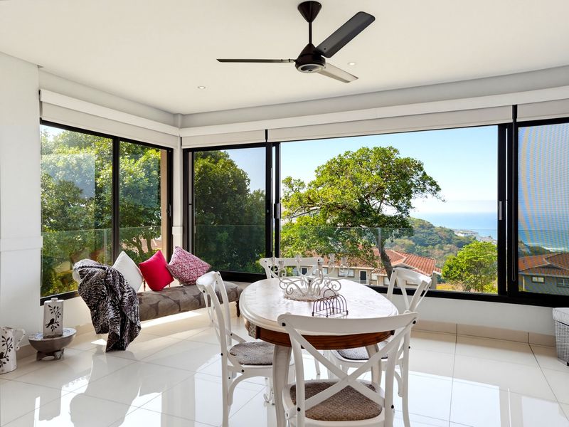 Bright dining area featuring large sliding glass doors, a modern ceiling fan, and expansive views of the surrounding landscape and ocean.