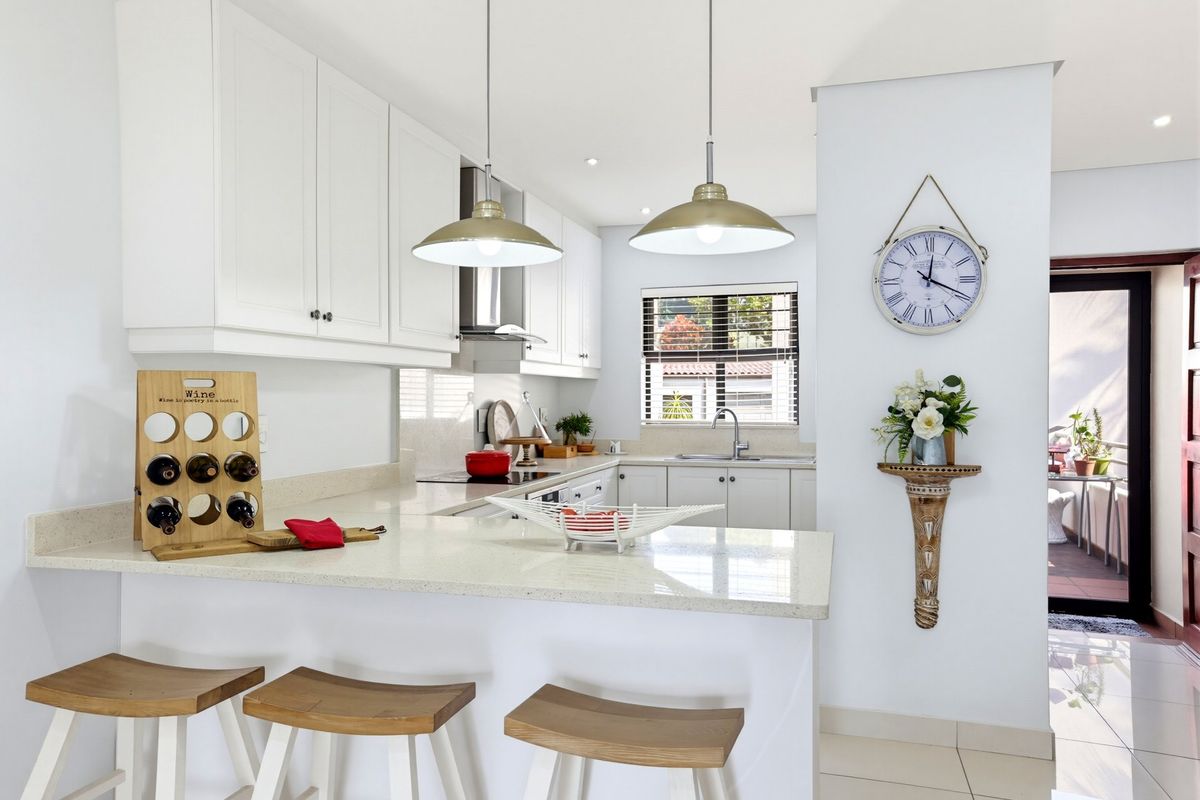 Modern kitchen featuring white shaker-style cabinetry, quartz countertops, stainless steel extractor fan, and stylish pendant lighting, creating a bright and functional culinary space.