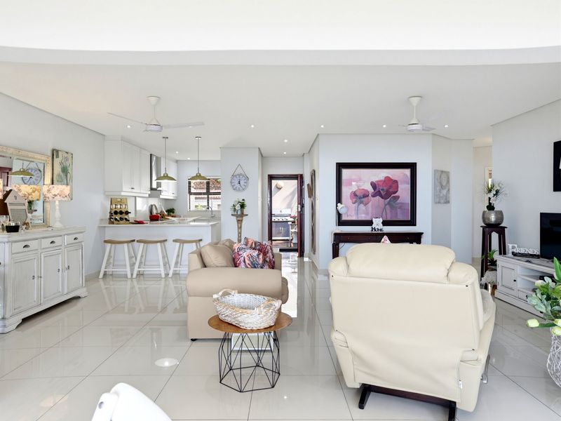Spacious open-plan living area featuring a modern kitchen with stone countertops, a central island, and bright, neutral tiled flooring throughout.