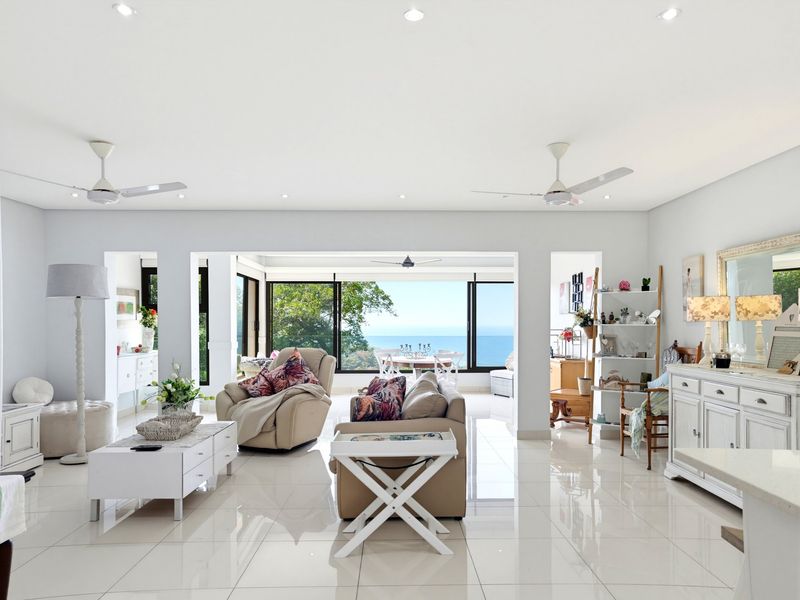 Spacious open-plan living area featuring polished tile flooring, recessed lighting, ceiling fans, and expansive glass doors offering scenic ocean views.