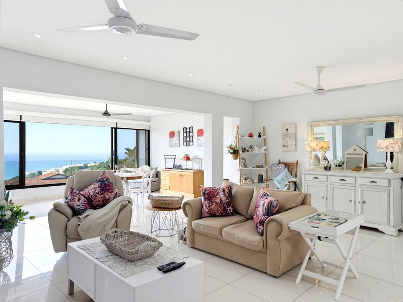 Spacious open-plan living area featuring tiled floors, recessed lighting, ceiling fans, and large sliding glass doors opening to a scenic coastal view.