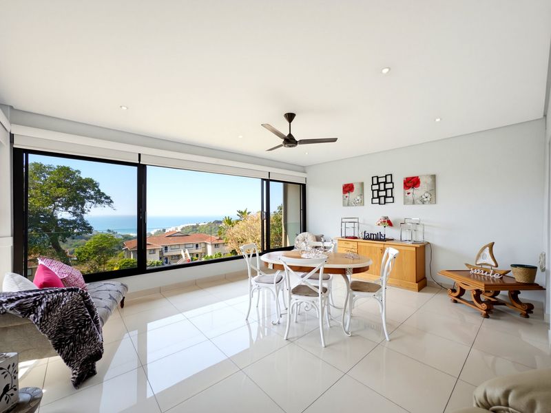 Bright open-plan living and dining area featuring large sliding glass doors that offer expansive coastal views and abundant natural light.
