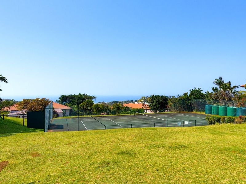 A well-maintained outdoor tennis court facility featuring perimeter fencing and adjacent water storage tanks, set within a landscaped residential estate.