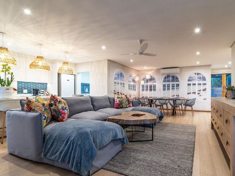 Spacious open-plan living and dining area featuring timber flooring, recessed lighting, and a modern kitchen with a tiled backsplash.