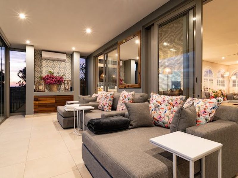 A modern, covered patio featuring tiled floors, recessed lighting, a split-system air conditioner, and decorative wall accents, seamlessly connected to the interior via sliding doors.