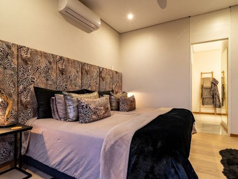 A well-maintained bedroom featuring hardwood flooring, recessed lighting, an integrated air conditioning unit, and a custom upholstered headboard.