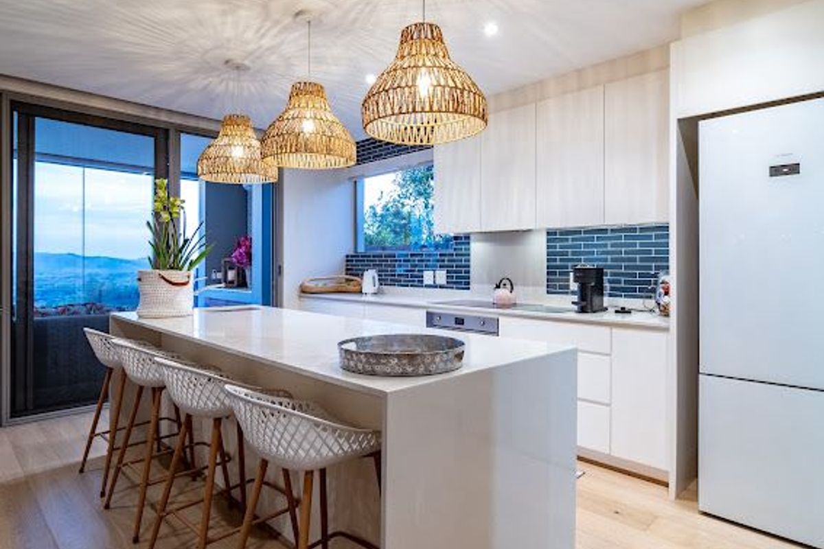 Modern kitchen featuring a large island with quartz countertops, sleek white cabinetry, subway tile backsplash, and integrated appliances, opening to a scenic balcony.
