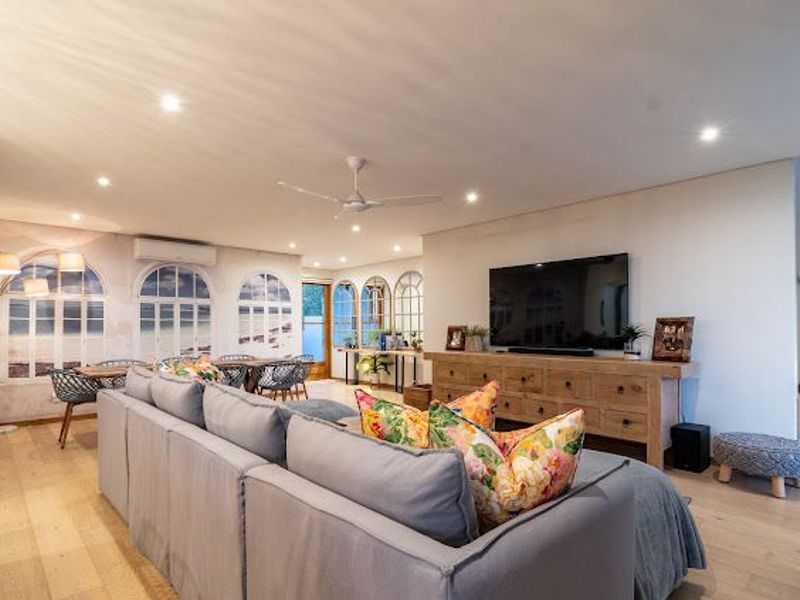 Spacious open-plan living area featuring timber flooring, recessed downlighting, a ceiling fan, and split-system air conditioning with decorative arched window features.