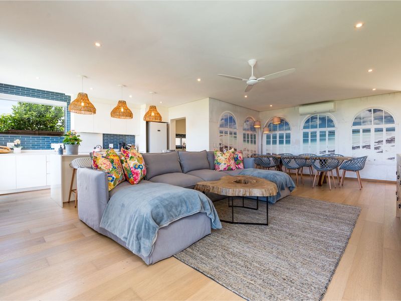 Spacious open-plan living and dining area featuring light timber flooring, a modern kitchen with blue subway tiles, and integrated climate control.