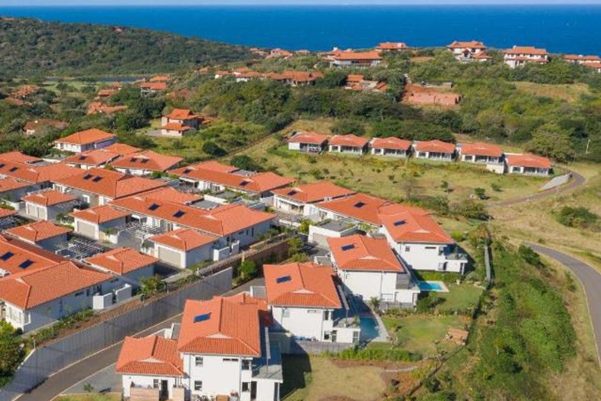 Aerial view of a residential estate featuring multiple detached homes with tiled roofs, private pools, and landscaped grounds overlooking the coastline.