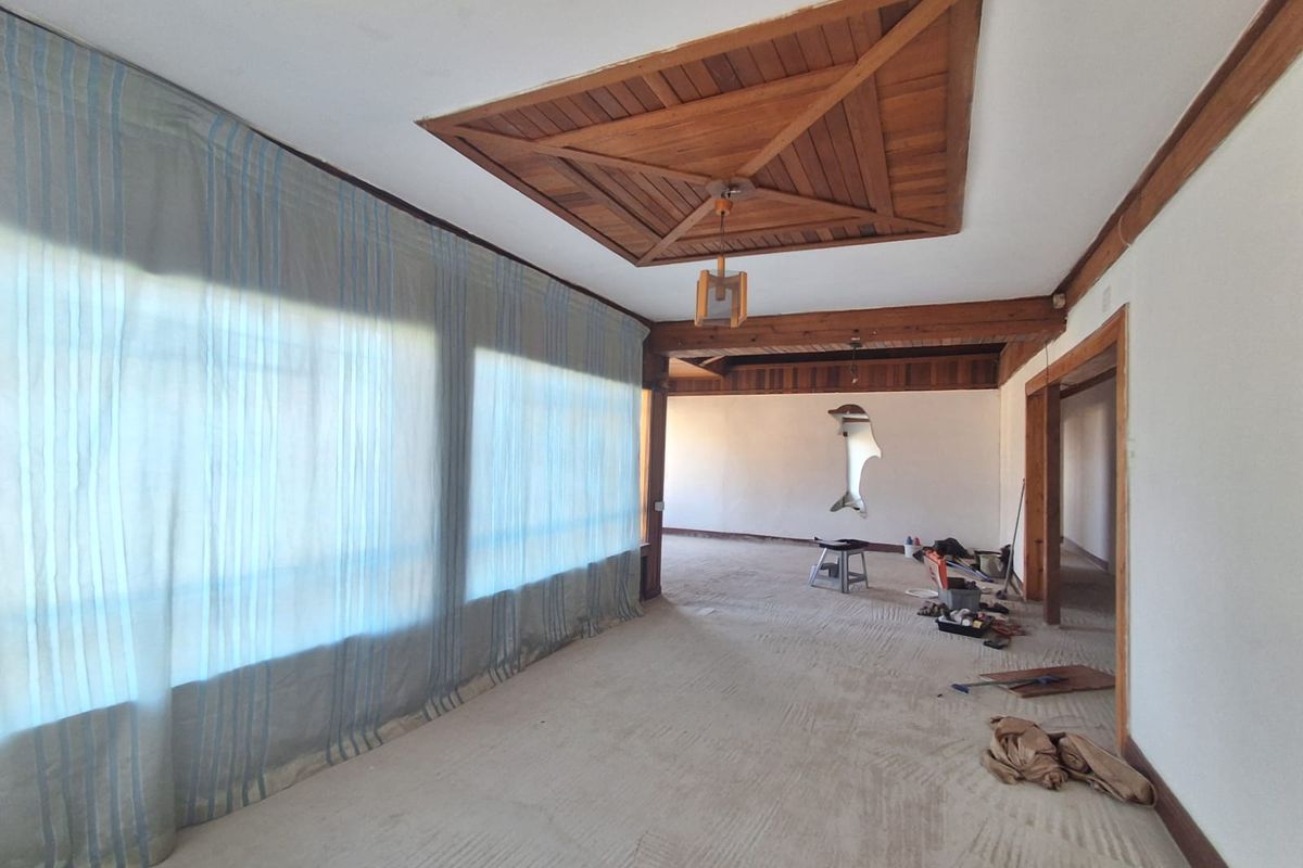 Spacious living area featuring a unique wooden ceiling design, exposed beams, and large windows, currently in need of cosmetic updates and repairs.