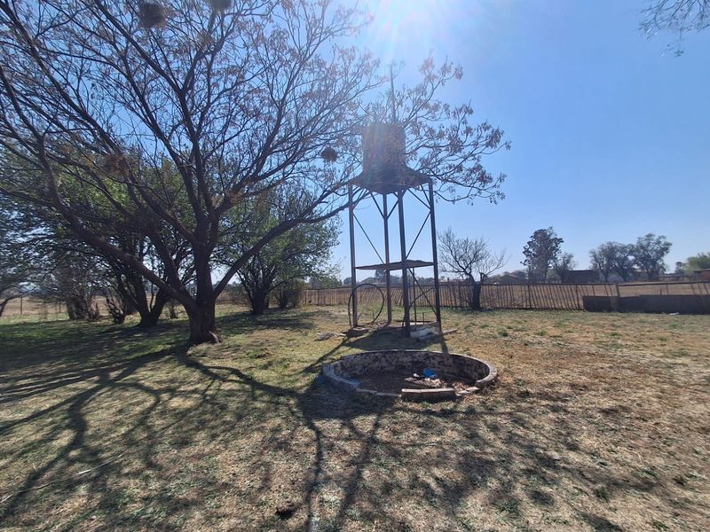 Outdoor farm area featuring a metal water tank stand and a circular brick reservoir set within a large open garden space.