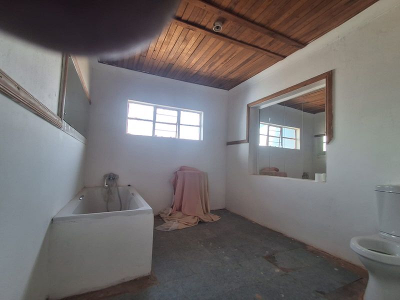 A dated bathroom featuring a built-in bathtub, toilet, and timber ceiling, requiring cosmetic updates to modernize the space.