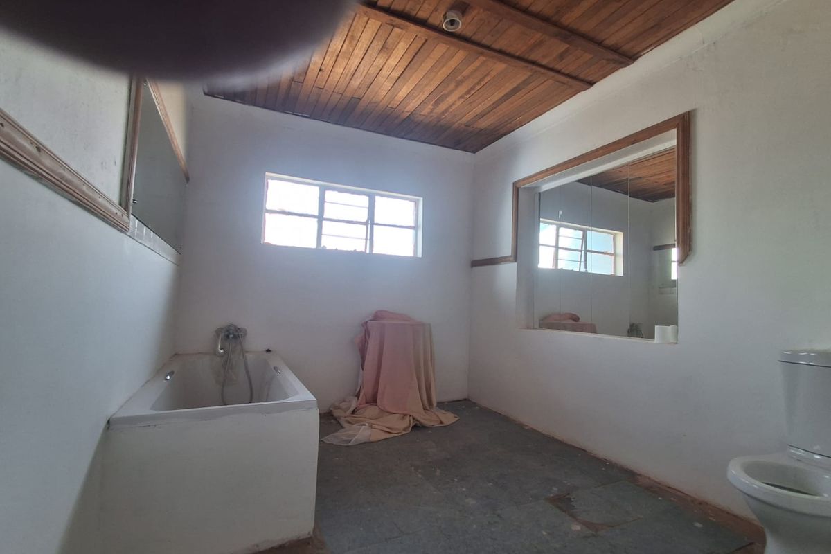 A dated bathroom featuring a built-in bathtub, toilet, and timber ceiling, requiring cosmetic updates to modernize the space.