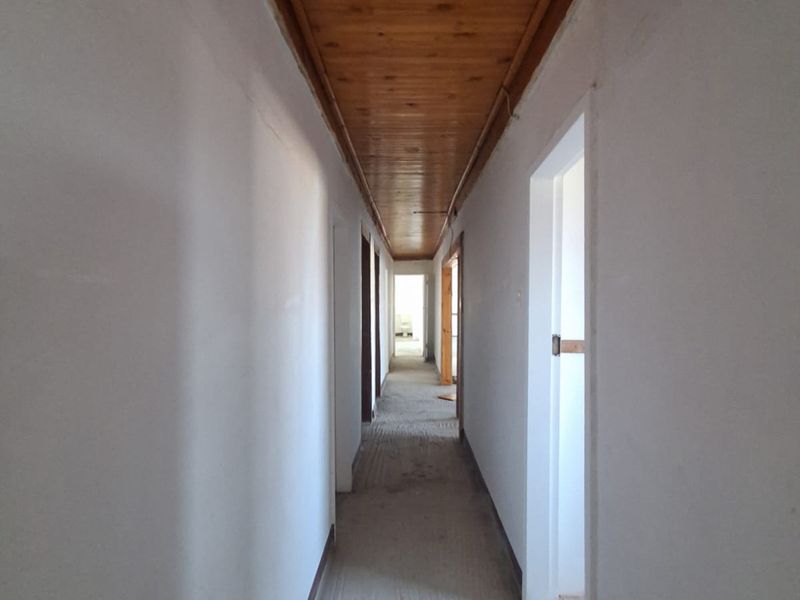 A long, empty hallway featuring a timber tongue and groove ceiling, requiring cosmetic updates to the flooring and wall finishes.