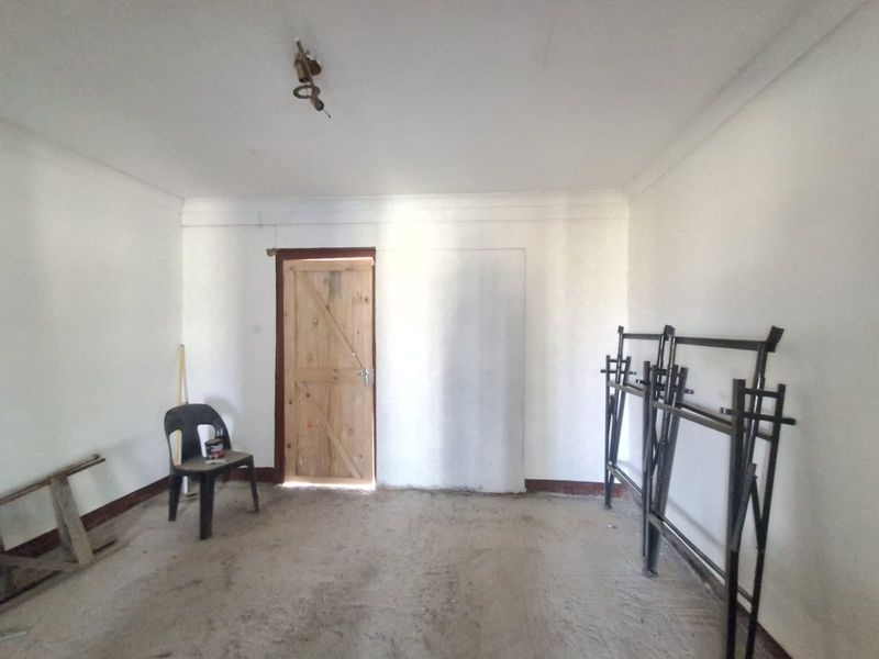 An unfinished bedroom space featuring a wooden door, exposed ceiling wiring, and raw concrete flooring, offering a blank canvas for renovation.