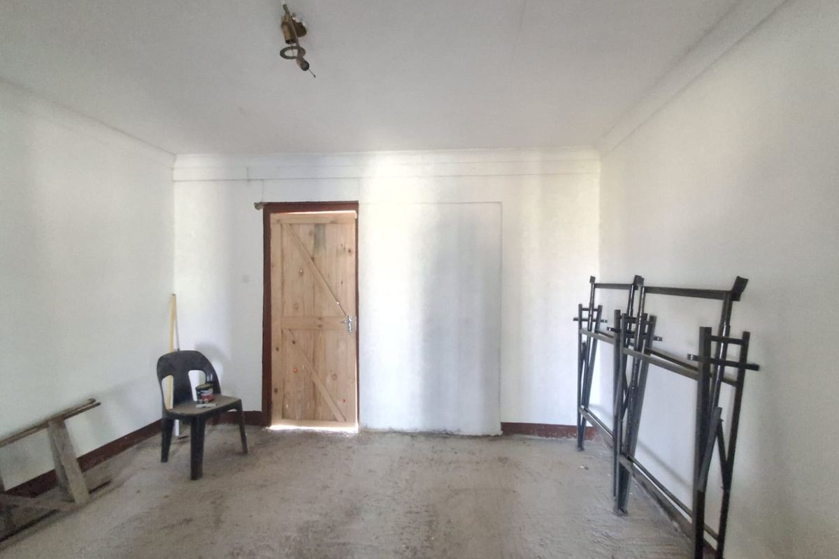 An unfinished bedroom space featuring a wooden door, exposed ceiling wiring, and raw concrete flooring, offering a blank canvas for renovation.