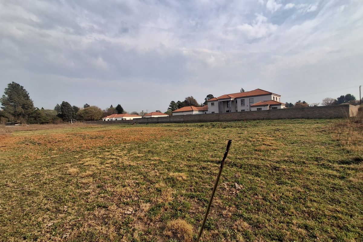 A view of a vacant residential plot featuring natural grassland and a perimeter boundary wall with neighboring properties in the background.