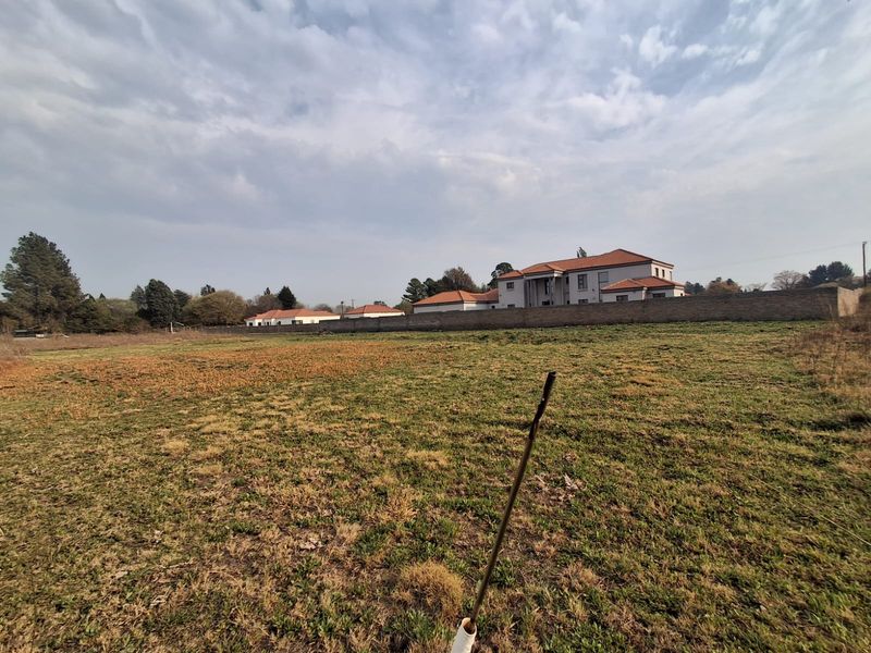 A view of a vacant residential plot featuring natural grassland and a perimeter boundary wall with neighboring properties in the background.