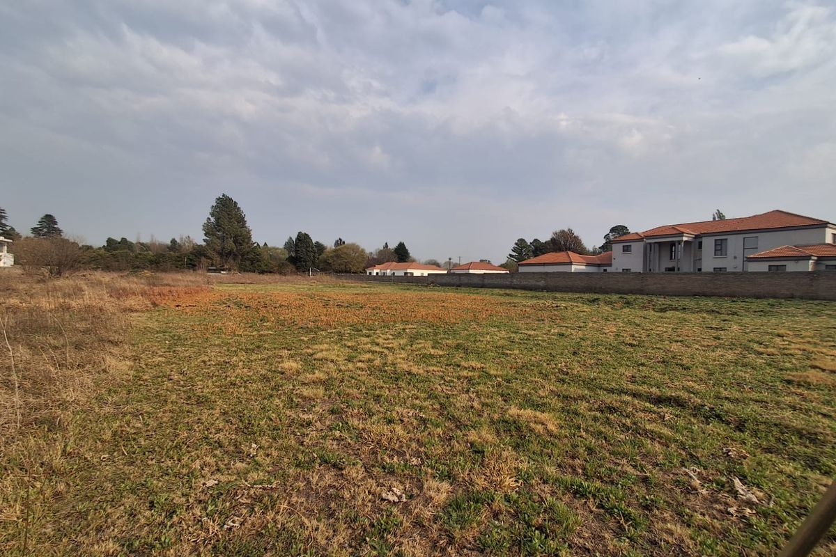 A vacant residential plot featuring open grass land and a perimeter boundary wall, situated in a developed neighborhood.