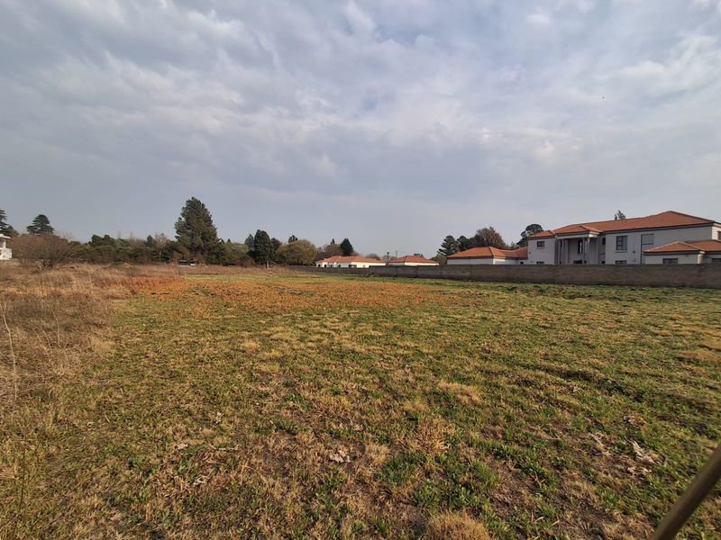 A vacant residential plot featuring open grass land and a perimeter boundary wall, situated in a developed neighborhood.