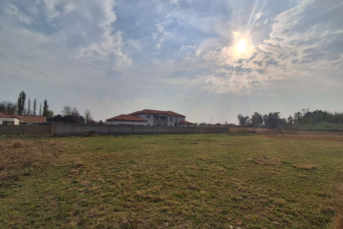 A wide-angle view of a vacant residential plot featuring natural grassland and a perimeter boundary wall with neighboring properties in the background.