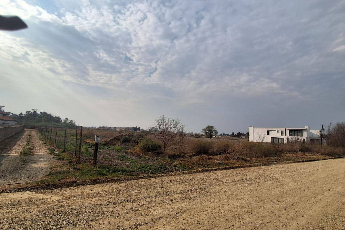 A view of an unimproved residential vacant lot from an unpaved gravel road, featuring wire perimeter fencing and open landscape.